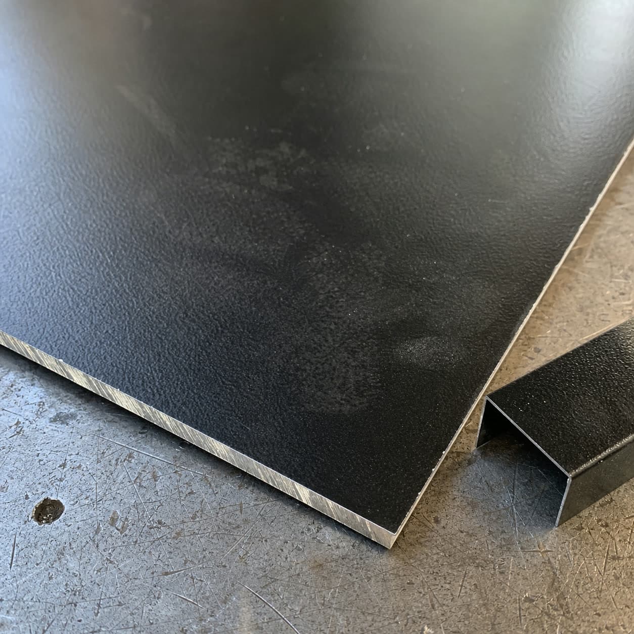 Detalle cercano de chapa negra prepintada texturada sobre una mesa de taller